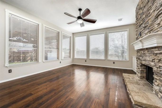 Move-out cleaning Spacious room with large windows, wood floors, and a stone fireplace.